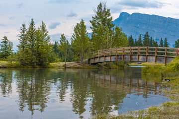 Fototapeta premium Cascade Ponds in Banff National Park during summer time with bridge in view and magpie on the lakeshore with towering Mount Rundle in view.