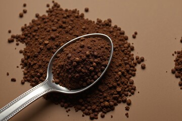 Ground Coffee Powder Spread Over a Brown Background with a Silver Spoon Scoop, Highlighting the Rich Aromatic Texture and Fine Granularity of the Brewed Beverage Ingredient