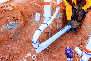 Worker is connecting PVC pipes in trench, ensuring proper alignment at construction location