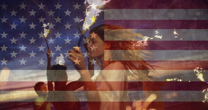 Image of friends dancing with sparklers on beach against american flag waving - Powered by Adobe