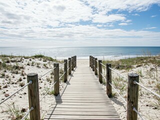 Obraz premium A wooden boardwalk leads to a serene beach, sunlight cast on the sand dunes, full of natural beauty.