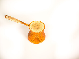 Turkish coffee pot (cezve) with foamy freshly brewed organic coffee isolated against a white background