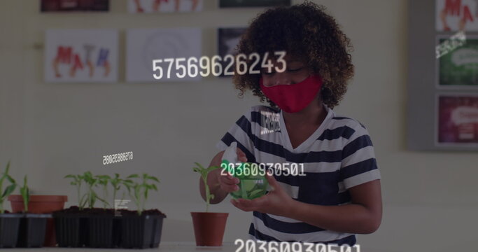 Image of rising numbers and schoolchild in class wearing face mask watering plant - Powered by Adobe