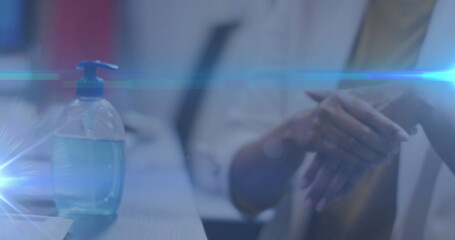 Blue light trails against mid section of woman using hands sanitizer at office