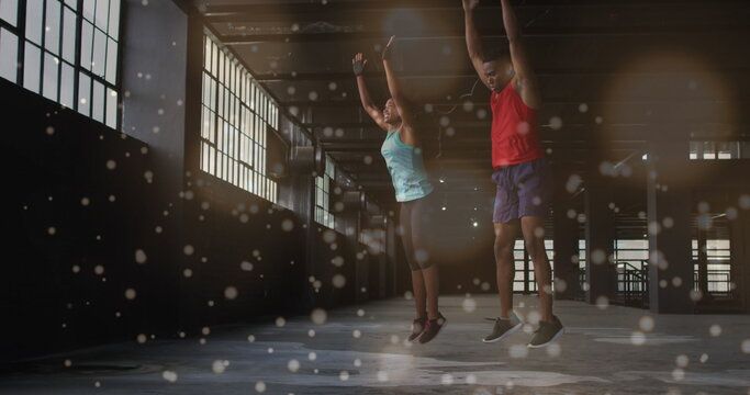 Image of spots flowing over man and woman doing burpees, exercising in gym - Powered by Adobe