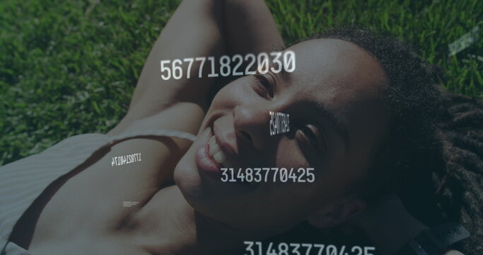 Image of numbers processing over happy woman lying on grass