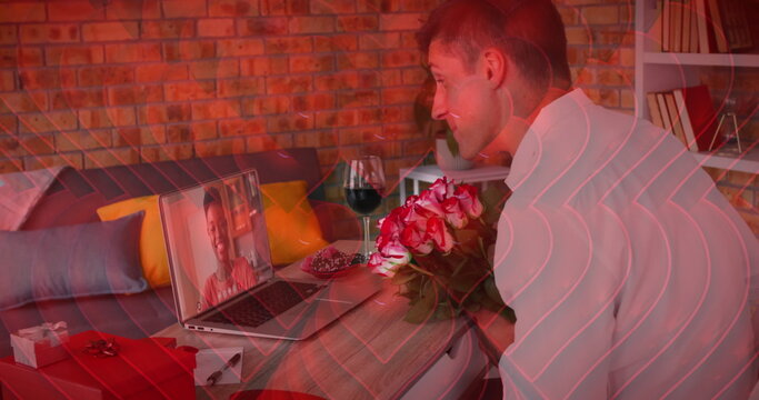 Red heart icons over caucasian man holding a flower bouquet while having a image call on laptop