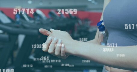 Multiple changing numbers against mid section of woman using hand sanitizer at the gym