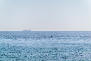 Calm blue sea with the silhouette of a large ship on the horizon