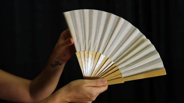 Close up static shot of hands opening and closing flamenco fan against black curtain