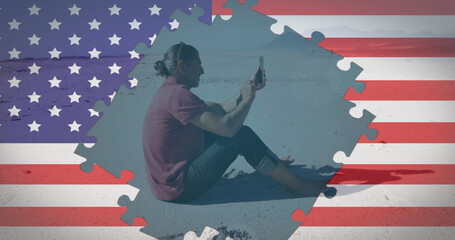Image of american flag jigsaw puzzles revealing man using smartphone sitting on beach