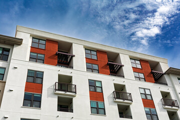 Upper floors of a contemporary apartment building red and white facade with large windows and balconies, set against a clear blue sky