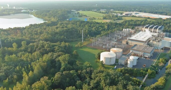 An energy production facility is surrounded by lush greenery, near a large lake and open fields.