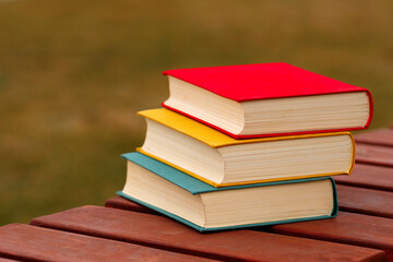 Close-up of three hardcover books stacked on wooden bench.