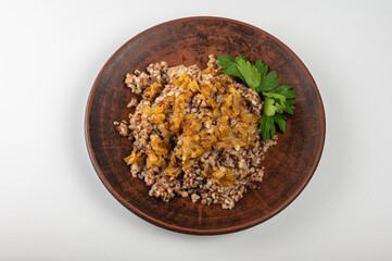 Traditional buckwheat porridge with caramelized onions on a rustic plate. A hearty, nutritious and aromatic dish, popular in Eastern European cuisine, on a clay plate, on a white background
