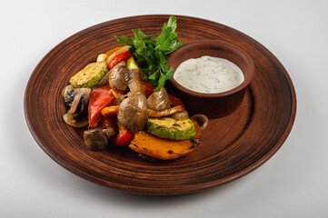 Delicious roasted vegetables on a rustic brown plate with creamy dipping sauce. Grilled zucchini, mushrooms, bell peppers, onions, and parsley garnish for a healthy meal