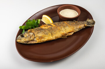 Crispy fried whole fish served on a brown plate with fresh parsley, lemon wedge and creamy sauce. A delicious seafood dish, perfect for a restaurant menu or food blog