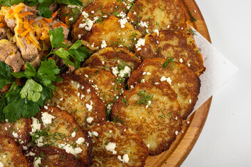 Traditional Belarusian or Ukrainian potato pancakes with fried meat, sauted vegetables, sour cream, cheese, mushroom sauce, and fresh herbs on a wooden platter