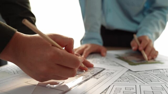 Smart architect and safety engineer discussion about building blueprint on table with architectural document, measurement tools and wooden block scatter around at modern office. Closeup. Delineation.