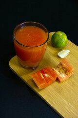 Papaya juice glass placed with lime on wooden board. Close-up ripe papaya mix with lime juice on black background. Pulp texture, healthy drink, eating, vegan, fresh fruit, ripe, and organic concept.