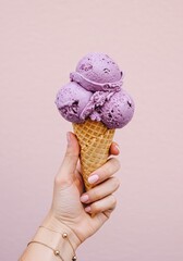 Hand holding triple scoop lavender ice cream cone against pastel background