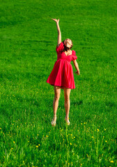 Woman in an elegant pink dress jumping on the green grass at sunset