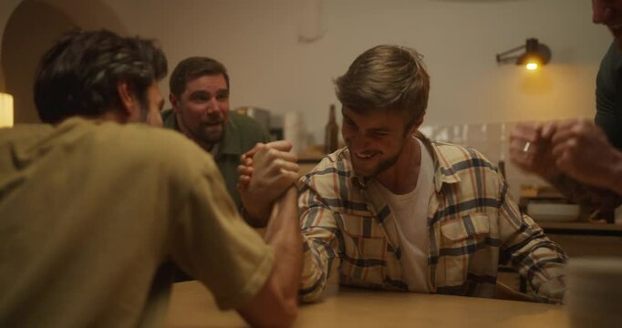 Two happy guys play arm wrestling while their friends support them at home during a bachelor party in the evening