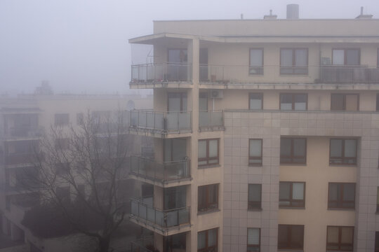 A thick fog blankets the city as seen from the balcony of an apartment building on a foggy early spring morning, with buildings barely visible in the mist.