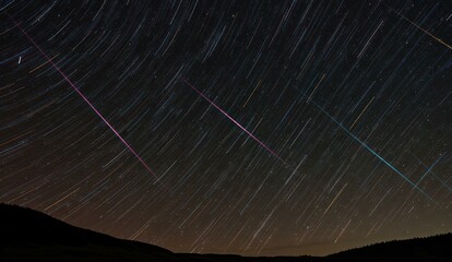 Night sky with star trails and meteors over a dark landscape,