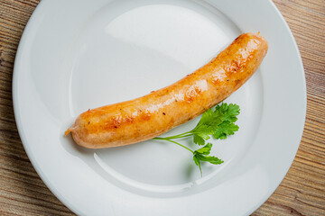 A single, golden-brown sausage is displayed on a white plate with a sprig of cilantro for garnish