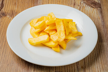 Delicious, golden potato fries piled high on a white plate against a warm, inviting wood backdrop