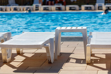 A row of white lounge chairs are set up on a patio next to a pool