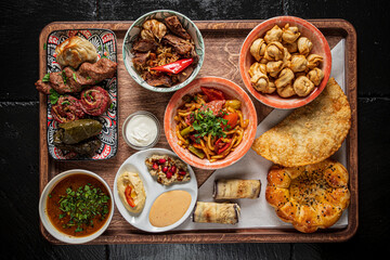 An assortment of vibrant dishes piled high on a wooden tray, showcasing rich flavors and textures