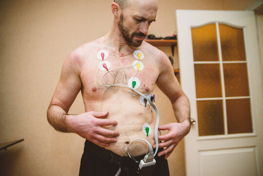 Man undergoing ECG EKG cardiac monitoring at home with electrode patches on chest. Medical heart rhythm monitoring with electrocardiogram sensors. Holter monitor testing for heart health assessment.