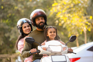 young indian family enjoy riding on scooter wearing helmet while traveling, Parents with young daughter on motorbike. Mode of transportation . © GAJENDRRA BHATI 
