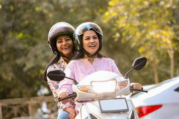 Two Carefree young indian women enjoy riding scooter wearing helmets. Friends having fun together ride motorbike, Transportation concept. © GAJENDRRA BHATI 