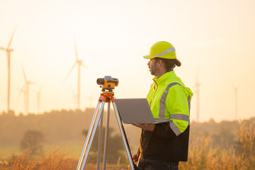 Engineer working on laptop in front of wind turbines for checking wind turbines of the field during beautiful sunset. Alternative energy concept.