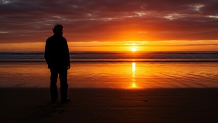 Fototapeta premium Silhouette of Caucasian senior man stands on sandy beach facing sunset over ocean. Waves gently lap at shore, vibrant colors evoke peacefulness and reflection.