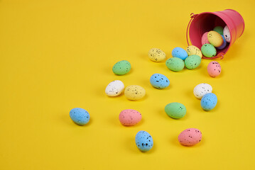 Easter eggs, pink bucket on a plain yellow background
