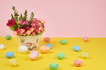 Pink flowers in a decorative bucket with three Easter eggs on a yellow and pink background