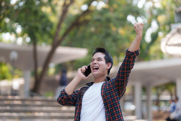 Fototapeta premium Excited young man receiving good news on smartphone, celebrating success outdoors