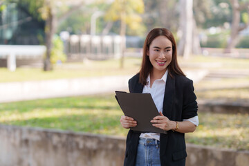 Obraz premium Smiling businesswoman holding documents in park: professional woman walking outdoors