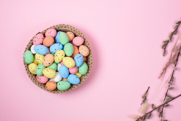 Obraz premium Willow twigs with colorful Easter eggs in a plate on a pink background, top view