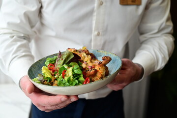 A close-up shot of gochujang chicken wings served with a colorful salad on a rustic plate in a restaurant setting.