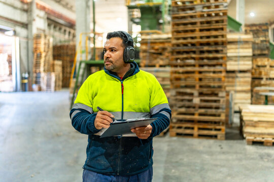 Man writing notes to clipboard in a carpentry recycling plant - Powered by Adobe