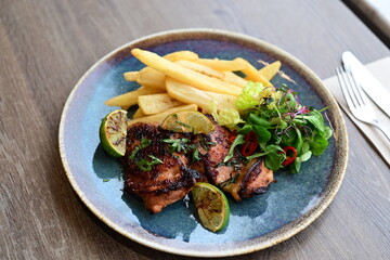 A plated serving of grilled Jamaican jerk chicken steak with crispy French fries and a fresh salad