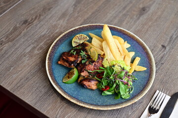 A plated serving of grilled Jamaican jerk chicken steak with crispy French fries and a fresh salad
