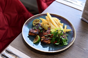 A plated serving of grilled Jamaican jerk chicken steak with crispy French fries and a fresh salad