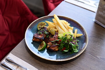 A plated serving of grilled Jamaican jerk chicken steak with crispy French fries and a fresh salad