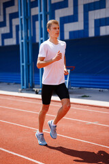Obraz premium Young male athlete sprinting on a red running track, wearing sportswear, training outdoors on a sunny day, focused on speed and performance.